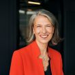 A professional woman wearing a red blazer and black top.